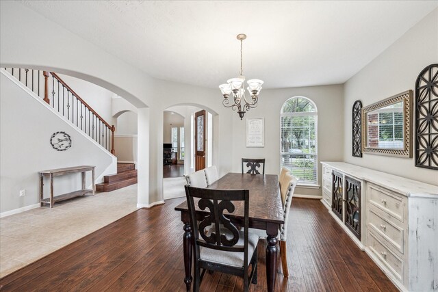dining room featuring dark wood-style flooring, arched walkways, stairway, baseboards, and a notable chandelier