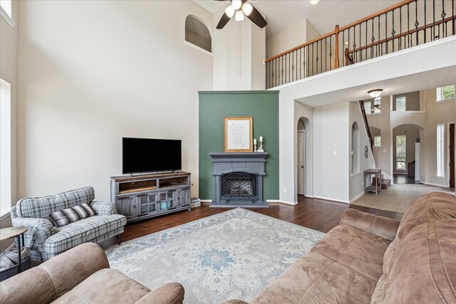 living room with wood finished floors, ceiling fan, a high ceiling, a fireplace with raised hearth, and arched walkways