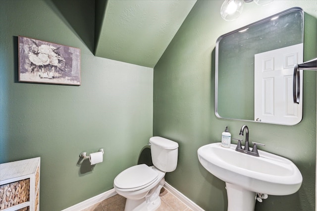 half bath with tile patterned flooring, lofted ceiling, toilet, baseboards, and a sink
