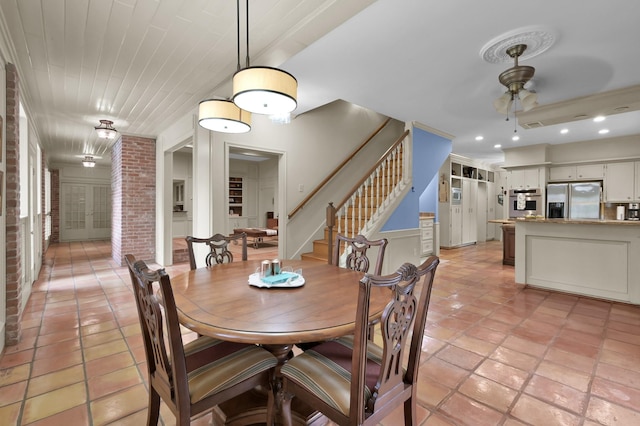dining room featuring stairway, brick wall, light tile patterned floors, ceiling fan, and a wainscoted wall