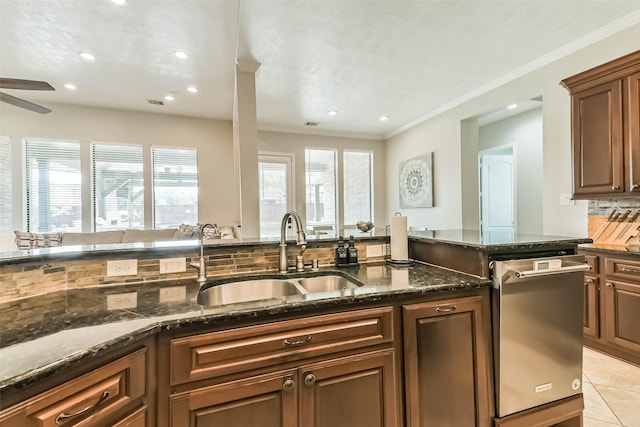 kitchen featuring dark stone countertops, a healthy amount of sunlight, dishwasher, and a sink