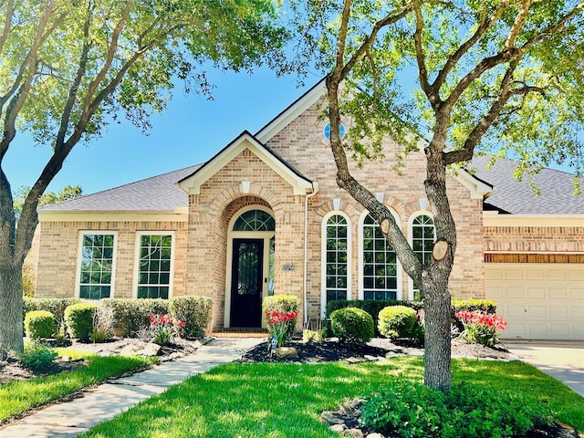view of front of home with brick siding, a shingled roof, a front yard, and a garage