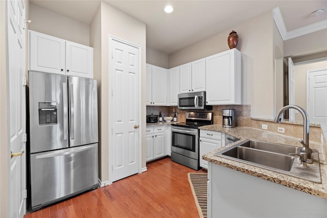 kitchen featuring tasteful backsplash, a sink, light wood-style flooring, white cabinets, and appliances with stainless steel finishes