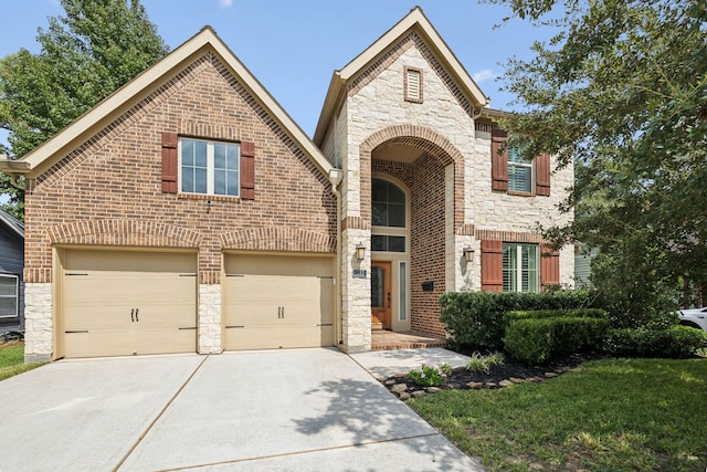 view of front of property featuring brick siding, an attached garage, driveway, and stone siding