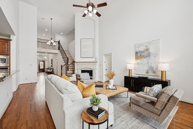 living area featuring a towering ceiling, wood finished floors, baseboards, stairway, and ceiling fan with notable chandelier