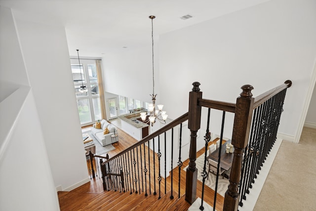 staircase with an inviting chandelier, baseboards, wood finished floors, and visible vents