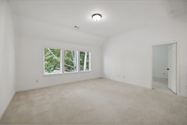 spare room featuring baseboards, light carpet, vaulted ceiling, and visible vents