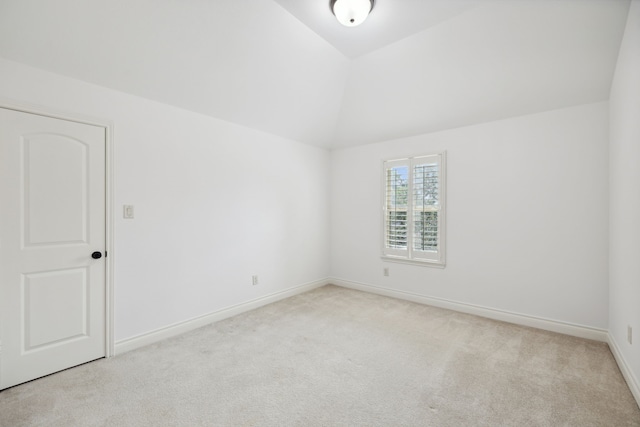 carpeted empty room featuring baseboards and vaulted ceiling