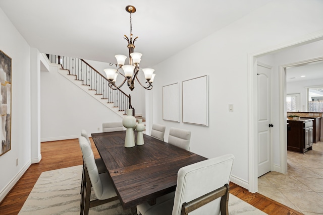dining area with light wood-type flooring, baseboards, a chandelier, and stairway