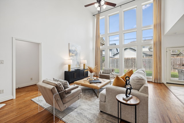 living room featuring wood finished floors, ceiling fan, baseboards, and a towering ceiling