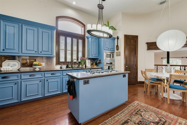 kitchen with a sink, appliances with stainless steel finishes, a kitchen island, blue cabinetry, and dark wood finished floors