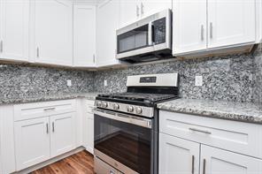 8926 Easthaven Blvd, Houston, TX 77075 - kitchen featuring light stone counters, stainless steel appliances, backsplash, white cabinetry, and dark wood-style flooring