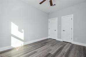 unfurnished bedroom with multiple closets, baseboards, a ceiling fan, and dark wood finished floors