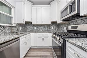 kitchen featuring light stone countertops, stainless steel appliances, a sink, and white cabinetry