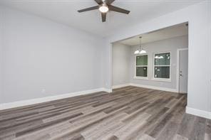 empty room featuring wood finished floors, baseboards, and ceiling fan with notable chandelier