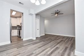 unfurnished living room featuring wood finished floors, visible vents, baseboards, and ceiling fan with notable chandelier