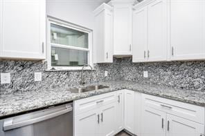 kitchen featuring white cabinets, a sink, backsplash, light stone counters, and dishwasher