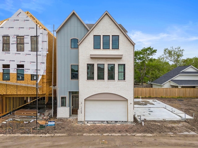 property in mid-construction featuring board and batten siding, an attached garage, brick siding, and fence