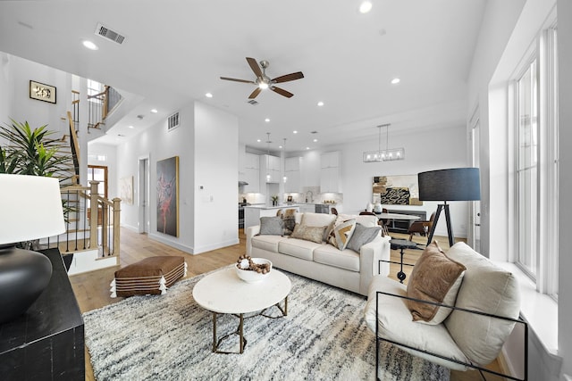 living room featuring light wood-type flooring, visible vents, recessed lighting, stairs, and ceiling fan