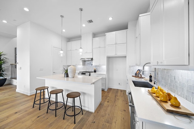 kitchen with backsplash, visible vents, a sink, gas range, and white cabinetry
