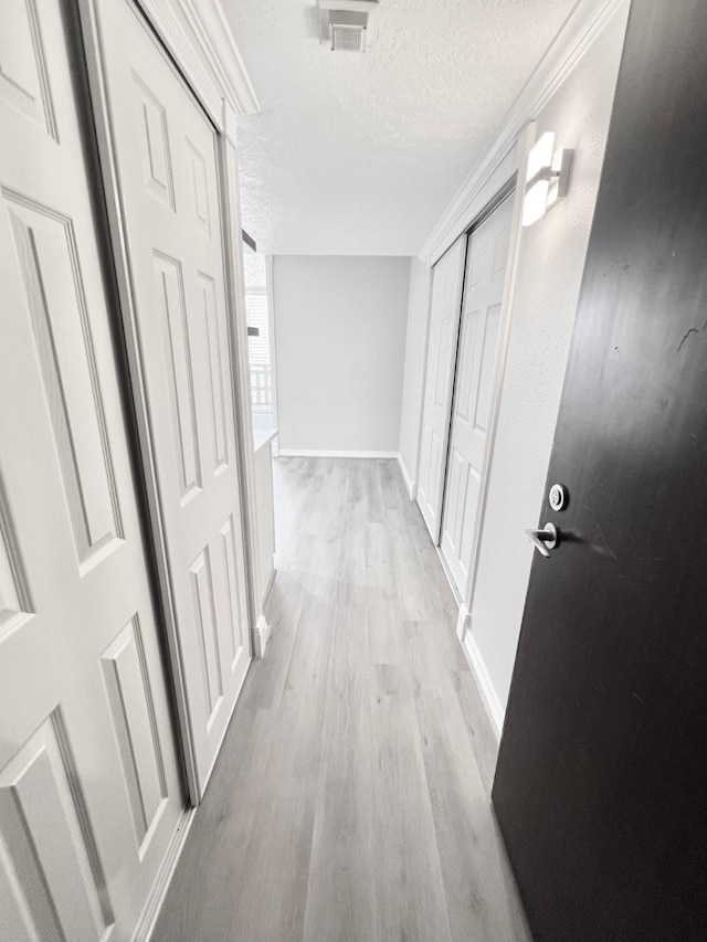 corridor featuring baseboards, visible vents, wood finished floors, and a textured ceiling