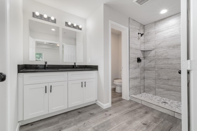 bathroom with wood finished floors, a sink, a tile shower, toilet, and visible vents