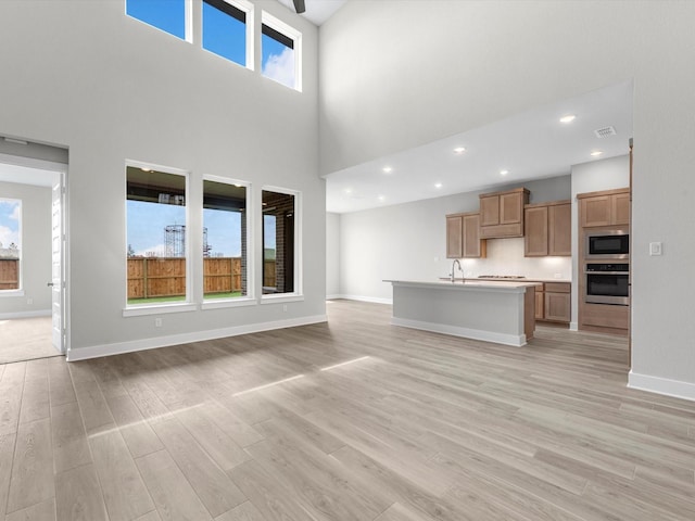 unfurnished living room featuring a high ceiling, light wood-style flooring, baseboards, visible vents, and recessed lighting