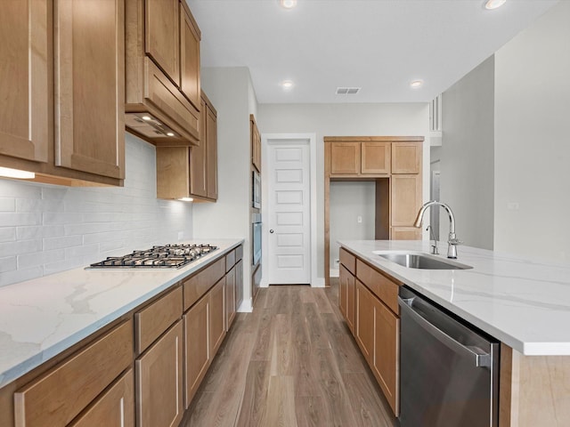 kitchen with a sink, backsplash, light wood-style floors, light stone counters, and appliances with stainless steel finishes