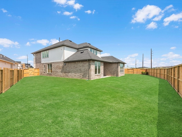 back of house featuring a lawn, a fenced backyard, brick siding, and roof with shingles
