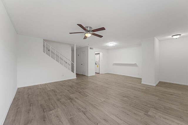 unfurnished living room with stairway, a ceiling fan, wood finished floors, baseboards, and visible vents