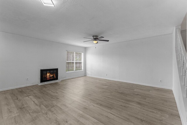 unfurnished living room featuring baseboards, wood finished floors, a fireplace, and ceiling fan