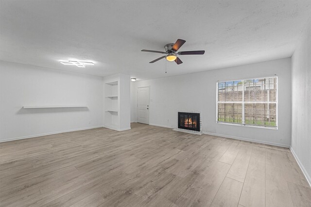 unfurnished living room with a ceiling fan, built in features, light wood-style flooring, a fireplace, and baseboards