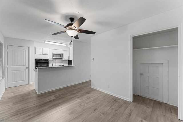 interior space featuring a sink, a textured ceiling, ceiling fan, light wood-style flooring, and baseboards