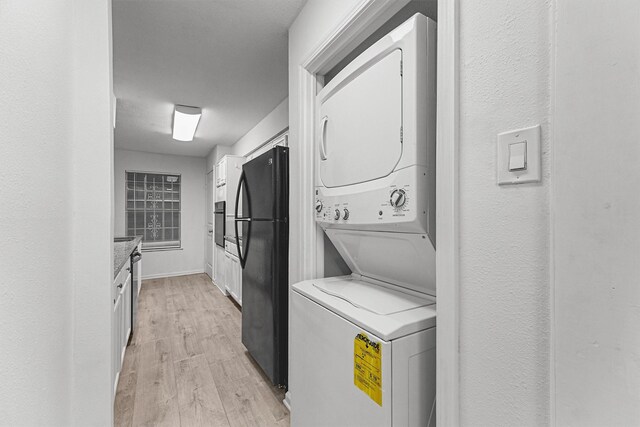 laundry room featuring light wood-type flooring, stacked washer and clothes dryer, and laundry area