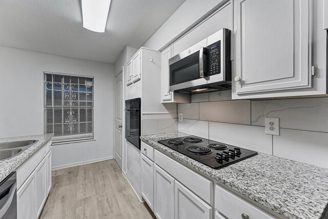 kitchen featuring white cabinets, light wood finished floors, light stone counters, black appliances, and tasteful backsplash