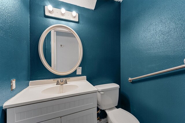 half bathroom with a textured wall, toilet, and vanity
