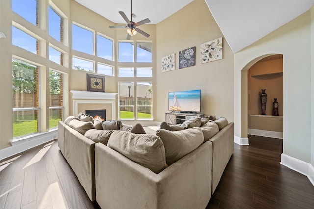 514 Whitney Oaks Ln, Stafford, TX 77477 - living area featuring dark wood-style flooring, a tiled fireplace, baseboards, a ceiling fan, and a high ceiling