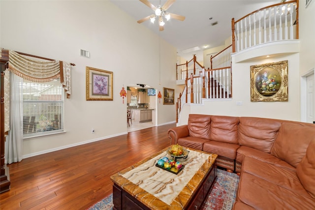 living area featuring visible vents, a ceiling fan, stairs, high vaulted ceiling, and wood-type flooring