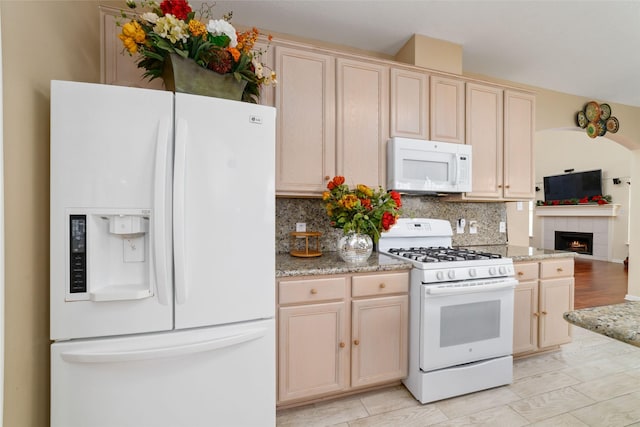 kitchen featuring tasteful backsplash, white appliances, light stone countertops, a fireplace, and cream cabinets