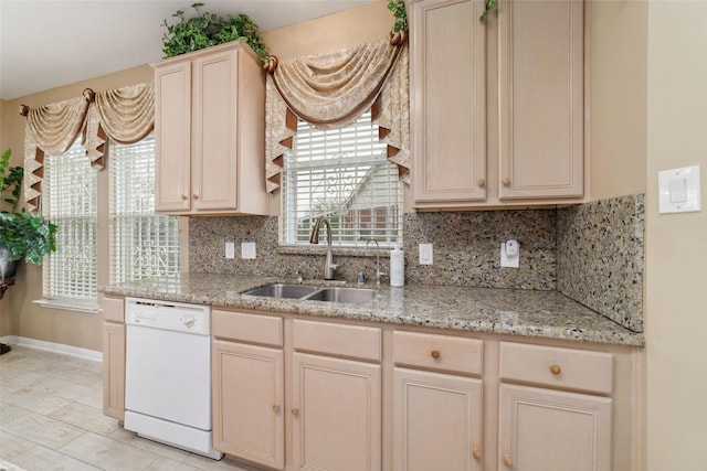 kitchen with light stone counters, tasteful backsplash, a sink, dishwasher, and baseboards