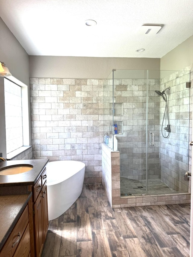 full bathroom with wood finished floors, a shower stall, vanity, and a soaking tub