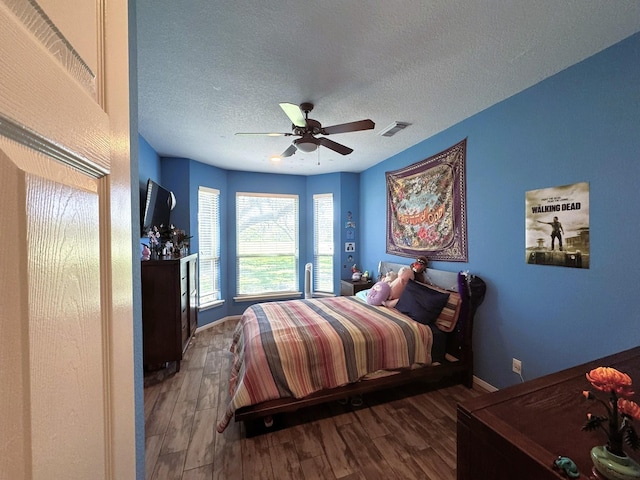 bedroom with a ceiling fan, visible vents, baseboards, a textured ceiling, and wood finished floors