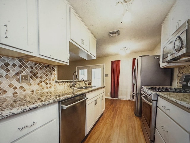 kitchen featuring white cabinets, stainless steel appliances, light wood-style flooring, a sink, and visible vents