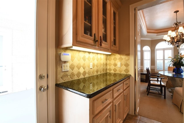 kitchen with crown molding, decorative backsplash, an inviting chandelier, dark countertops, and glass insert cabinets