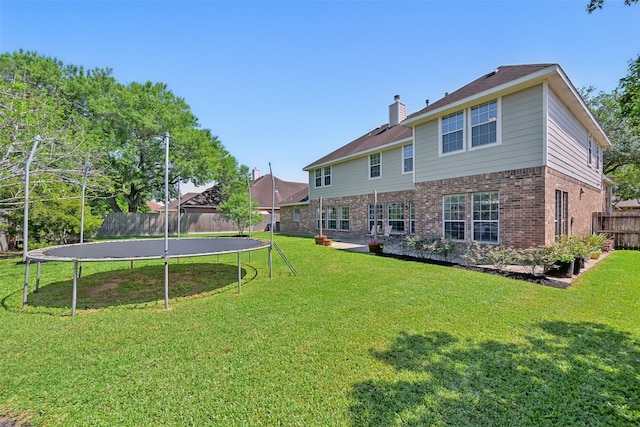 back of house featuring a trampoline, a chimney, a lawn, fence, and brick siding