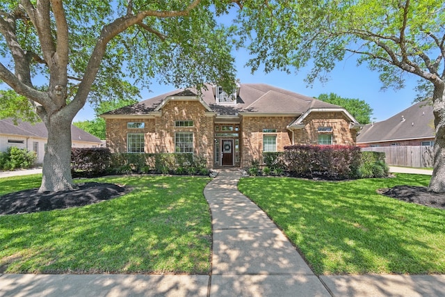 view of front facade featuring brick siding, roof with shingles, a front lawn, and fence