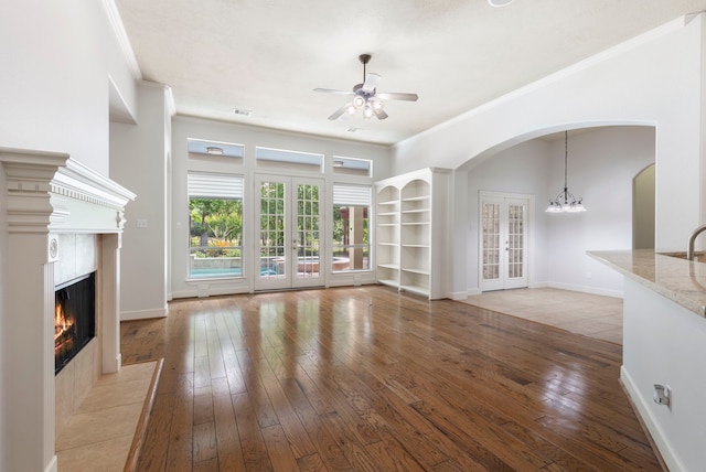 1614 Beau Rivage, Conroe, TX 77304 - unfurnished living room with french doors, a ceiling fan, ornamental molding, a fireplace, and arched walkways