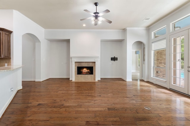 1614 Beau Rivage, Conroe, TX 77304 - unfurnished living room with arched walkways, a ceiling fan, dark wood-type flooring, a tiled fireplace, and crown molding