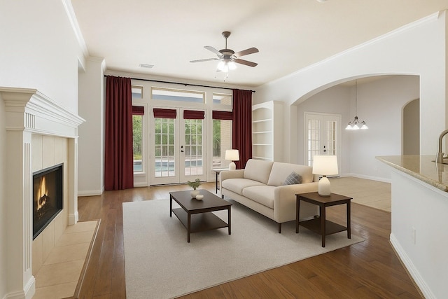1614 Beau Rivage, Conroe, TX 77304 - living room with arched walkways, ceiling fan, a tiled fireplace, ornamental molding, and wood finished floors