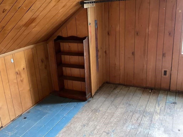 bonus room with light wood-type flooring, vaulted ceiling, and wood walls